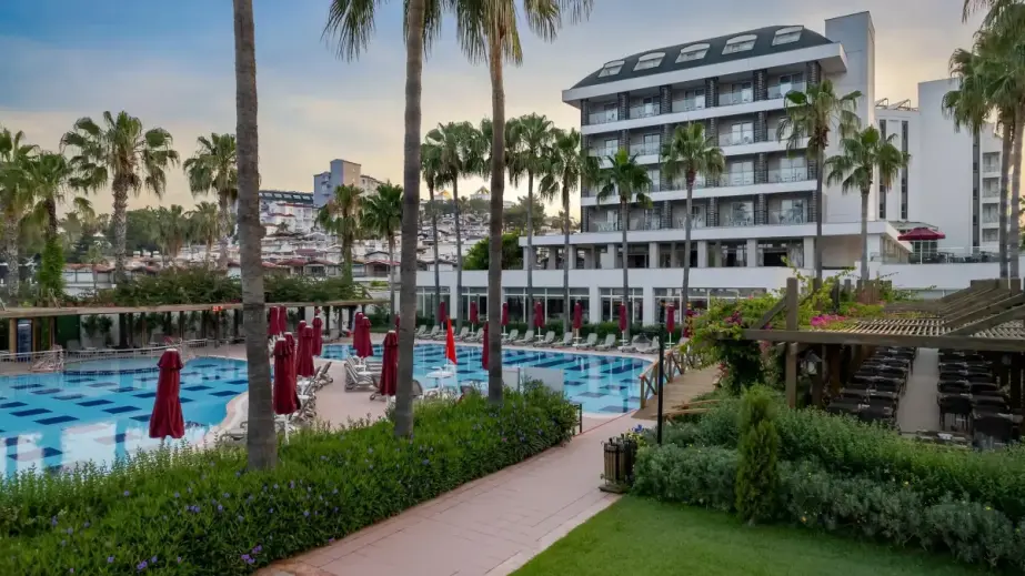 Trendy Palm Beach Gesamtansicht mit Pool, Tischen, Palmen, Hotelgebäude und Grünflächen