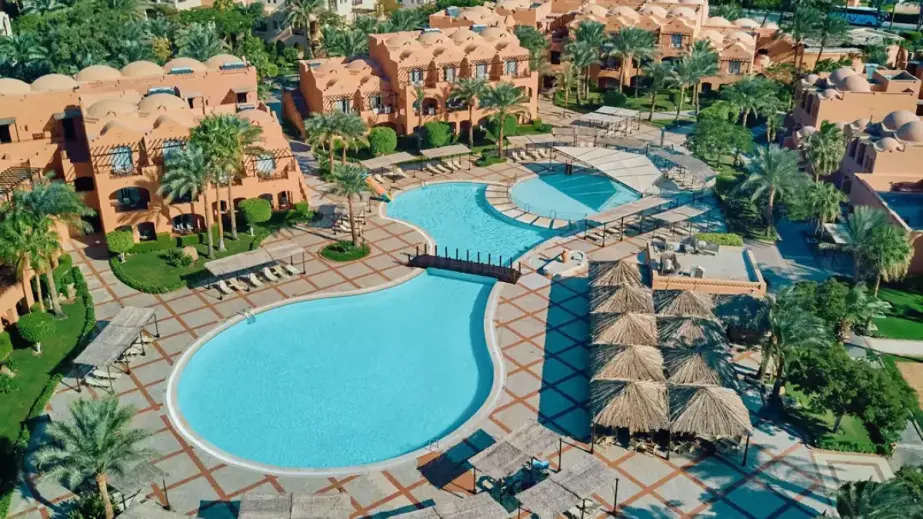 Jaz Makadi Oasis Resort Poolbereich mit Sonnenliegen, Poolbar, Palmen und Grünanlagen