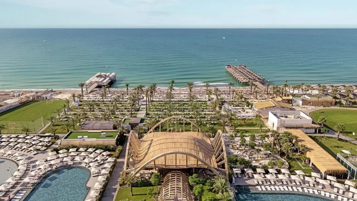Cabanas, sunbeds, umbrellas, palm trees, green areas, a pool, a lightly wavy sea and a pier in Belek