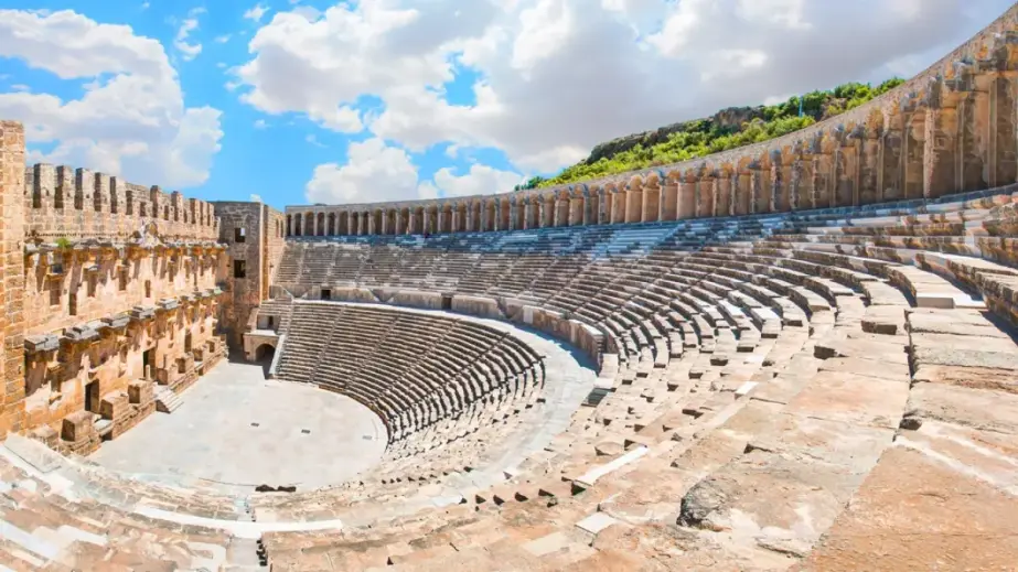 Sitzreihen des antiken Theaters von Aspendos unter bewölktem Himmel mit Grünflächen