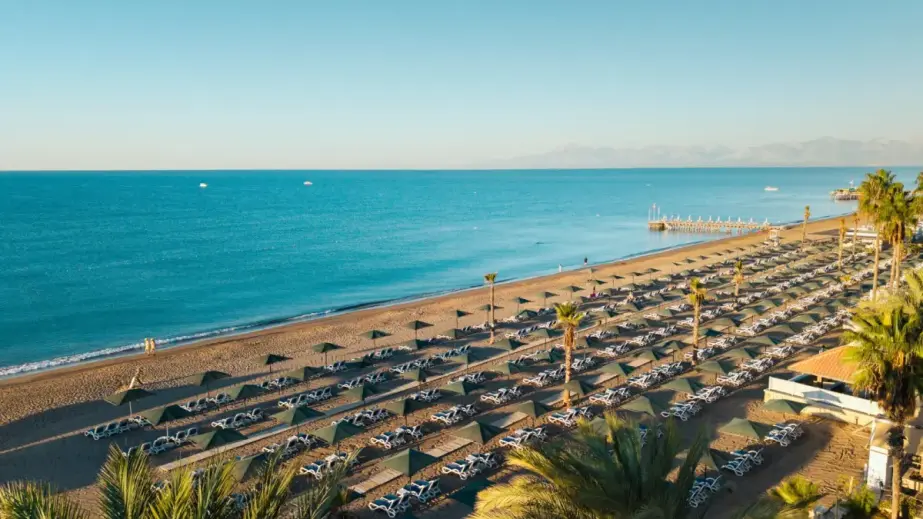 Cabanas, sunbeds, umbrellas, palm trees, a pier, boats and mountain views on Belek beach